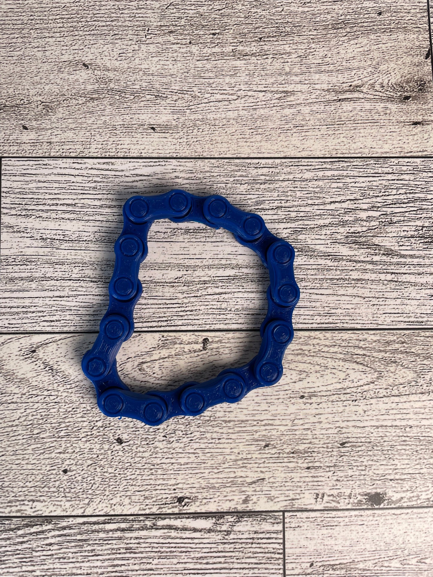 A blue chain link on a wood backdrop. The chain is arranged in a circle shape and there are eight links.