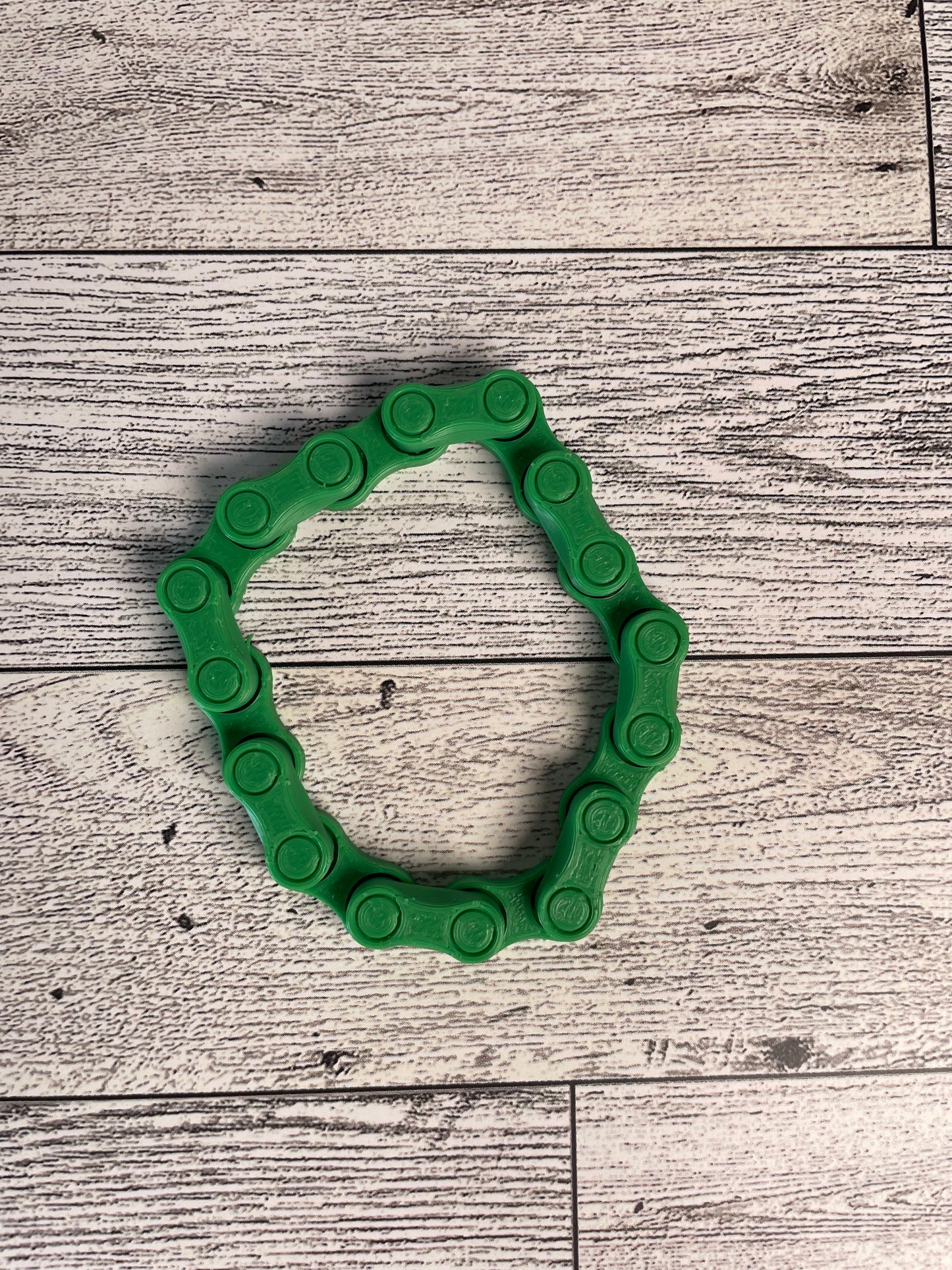A green chain link on a wood backdrop. The chain is arranged in a circle shape and there are eight links.