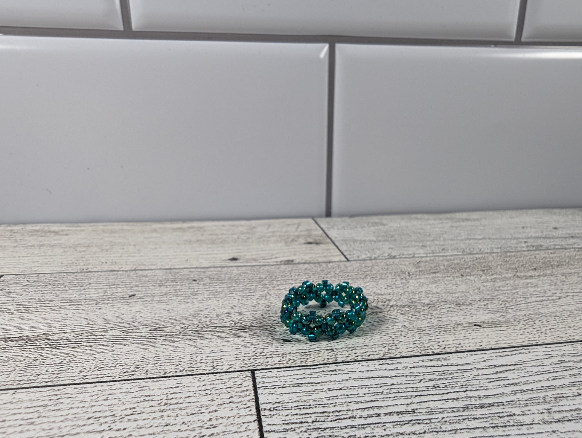 A green ring placed on a wood grain surface with a tile backdrop.