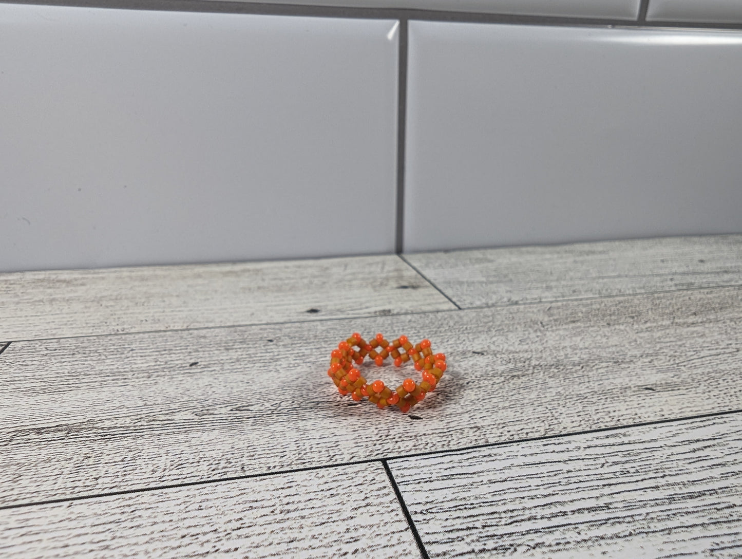 A orange ring with two shades placed on a wood grain surface with a tile backdrop.