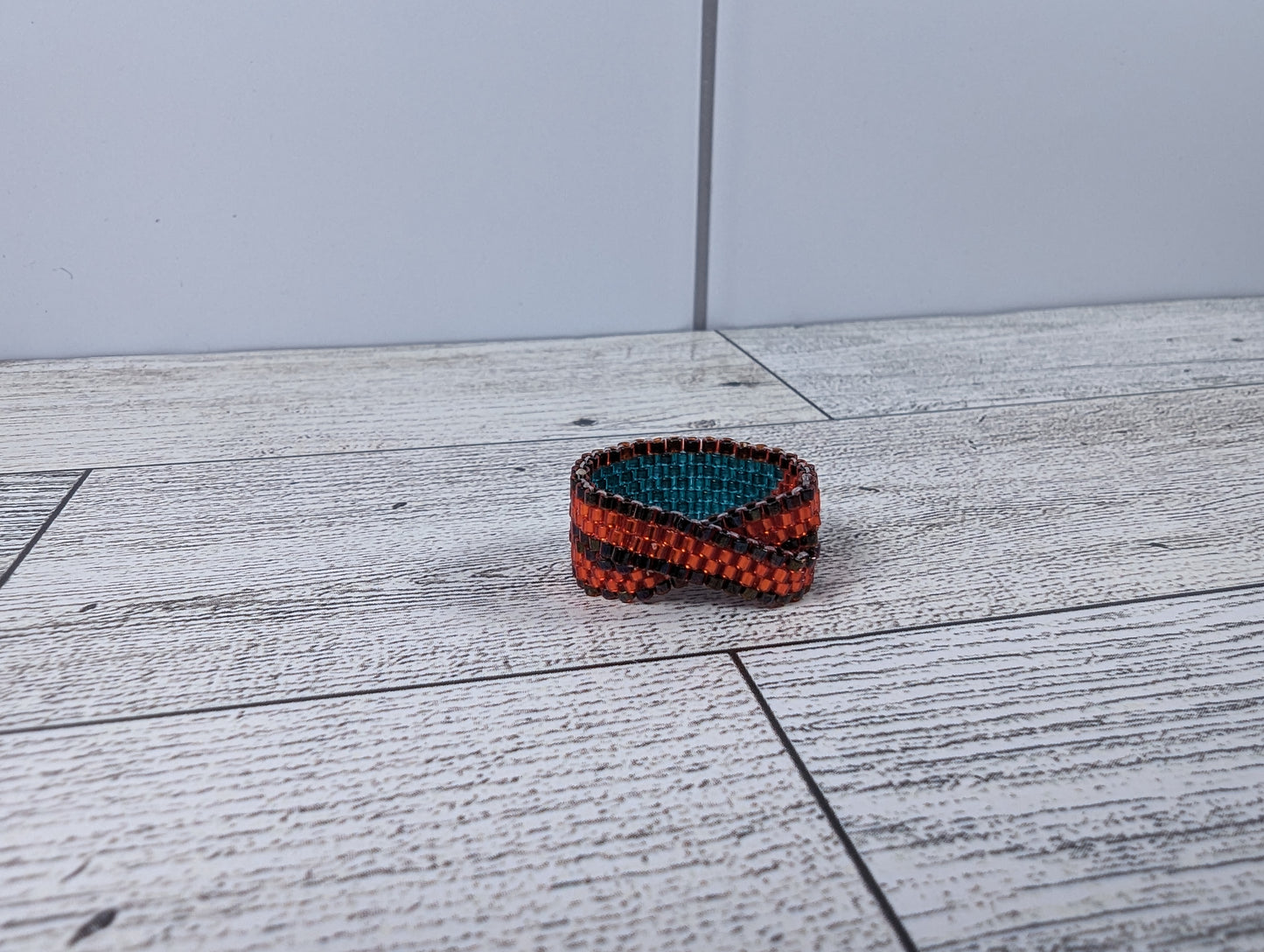 A red, blue, and black infinity ring placed on a wood grain surface with a tile backdrop.