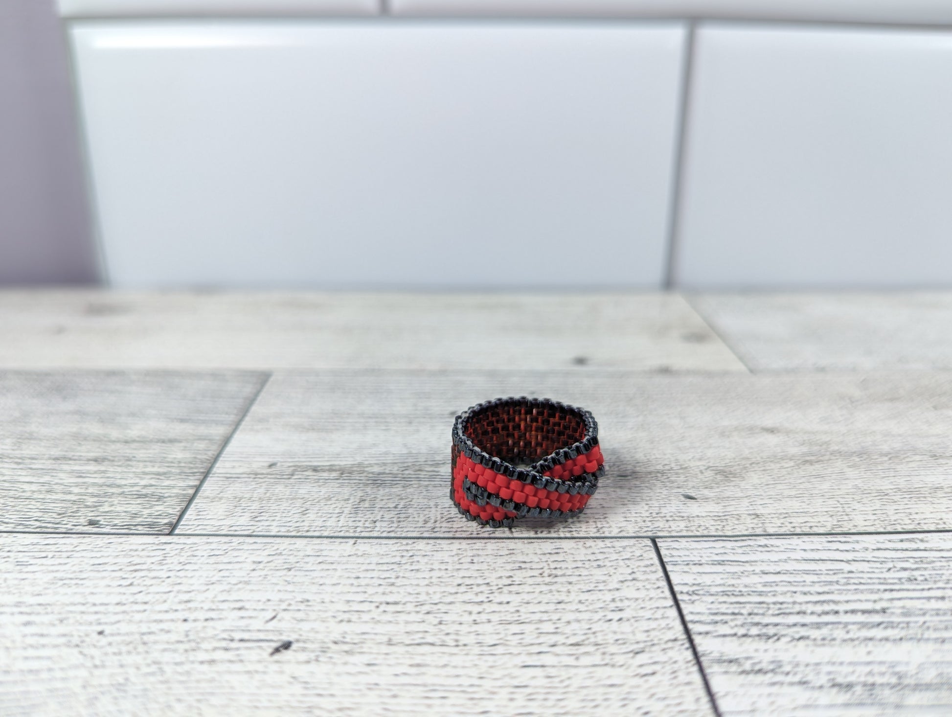 A red and black infinity ring placed on a wood grain surface with a tile backdrop.
