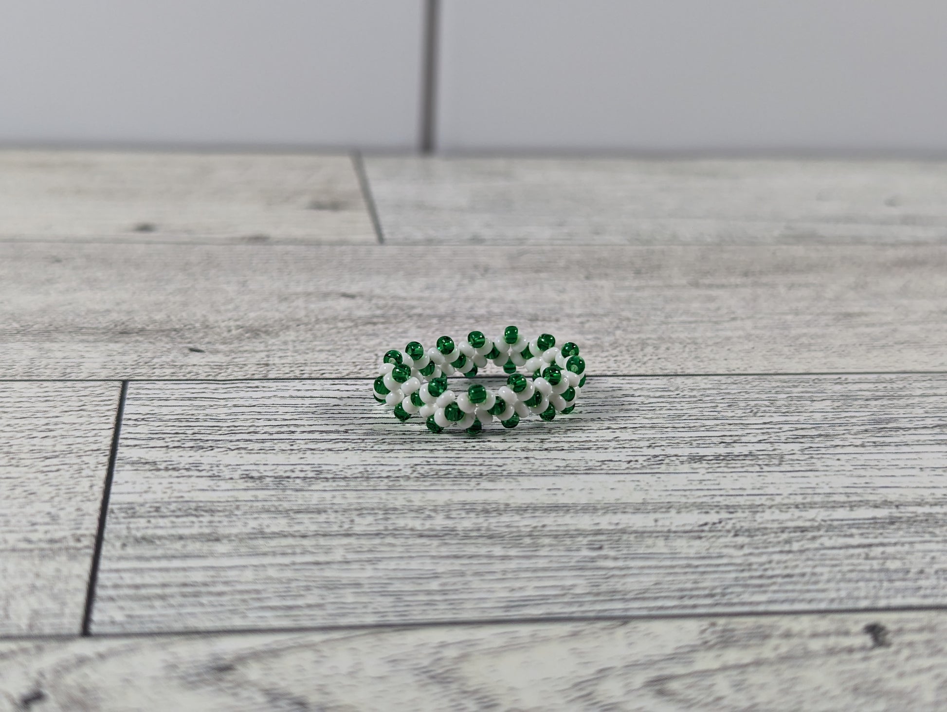 A green and white ring placed on a wood grain surface with a tile backdrop.