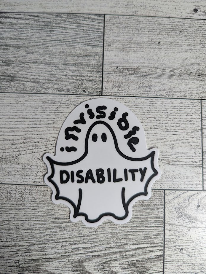 A ghost sticker with the word "invisible" drawn in squiggle font above and "DISABILITY" is across the wingspan. The ghost's arms are bat-like shape into the body. There is a light wood backdrop.