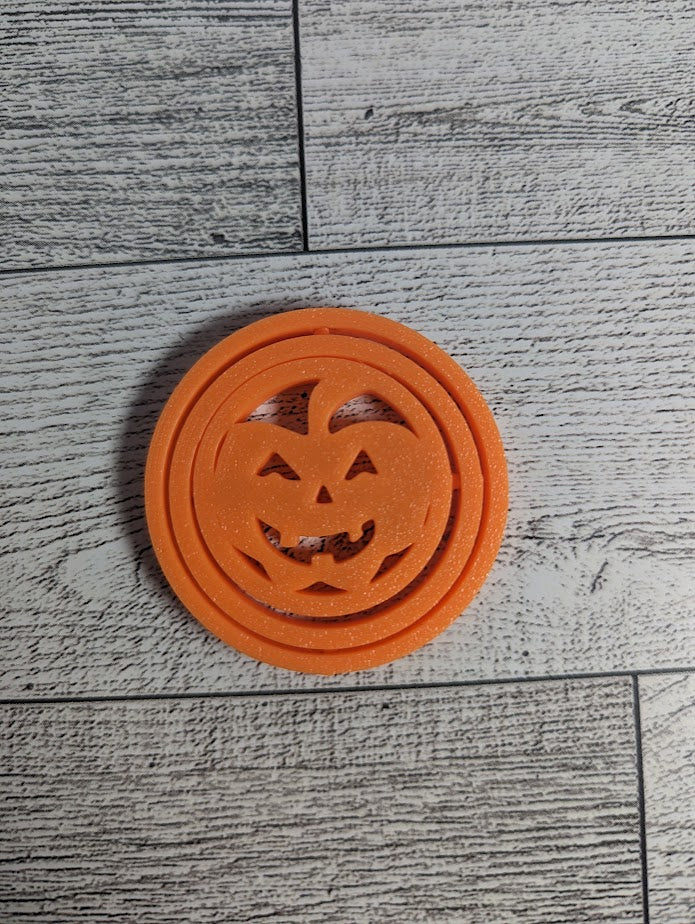 An orange circle jack-o-lantern fidget lies flat on a light wood grain