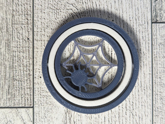 A white and grey Spider spinner laying flat on a light woodgrain