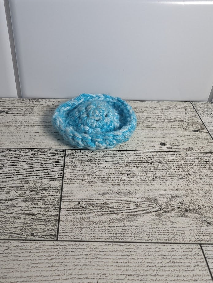 A crochet fidget with a light blue center and a light blue rim. The shape of the fidget resembles a sombrero. The background is a light wood grain and a white tile.