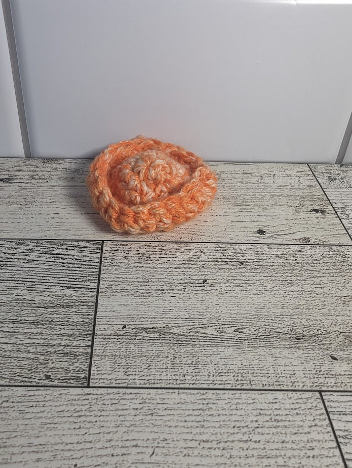 A crochet fidget with both an orange center and orange rim. The shape of the fidget resembles a sombrero. The background is a light wood grain and a white tile.