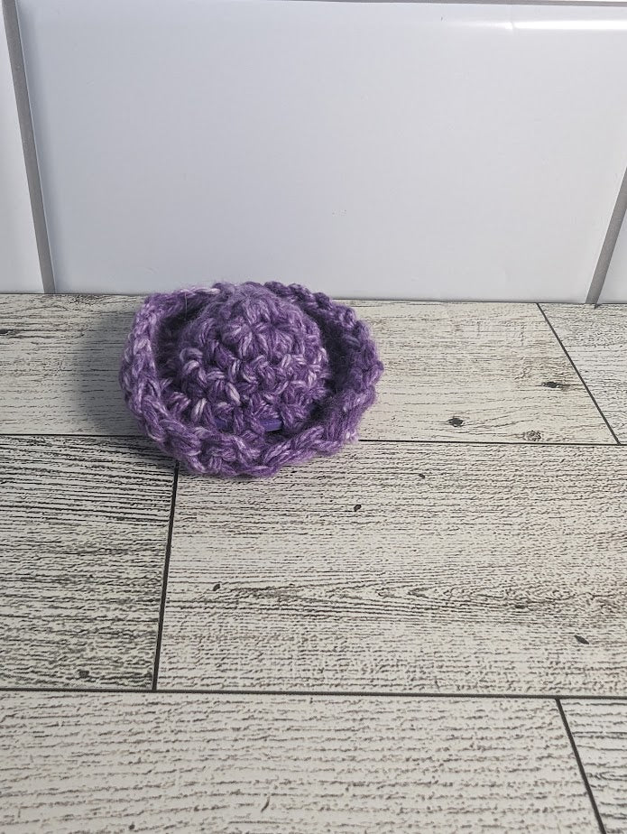 A crochet fidget with a purple center and a purple rim. The shape of the fidget resembles a sombrero. The background is a light wood grain and a white tile.