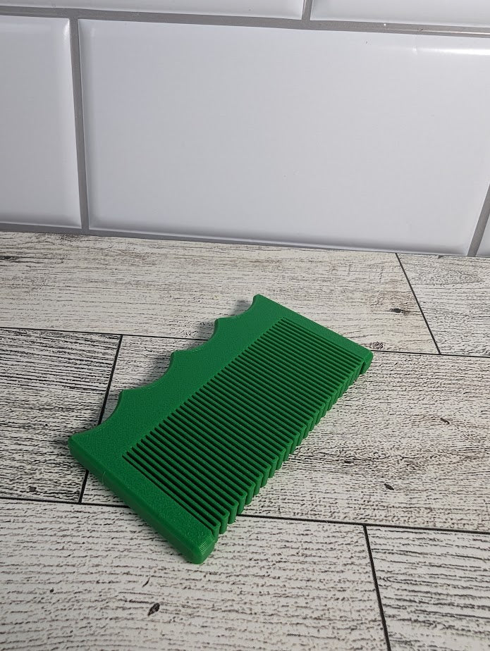 A green comb is on a light wood grain surface. The backdrop is a white tile