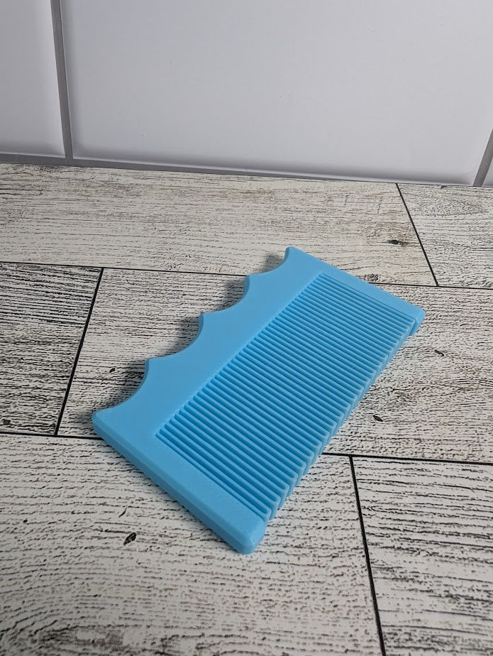 A light blue comb is on a light wood grain surface. The backdrop is a white tile