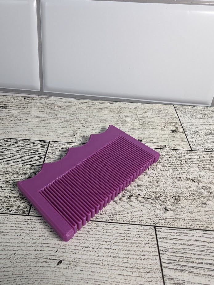 A magenta purple comb is on a light wood grain surface. The backdrop is a white tile