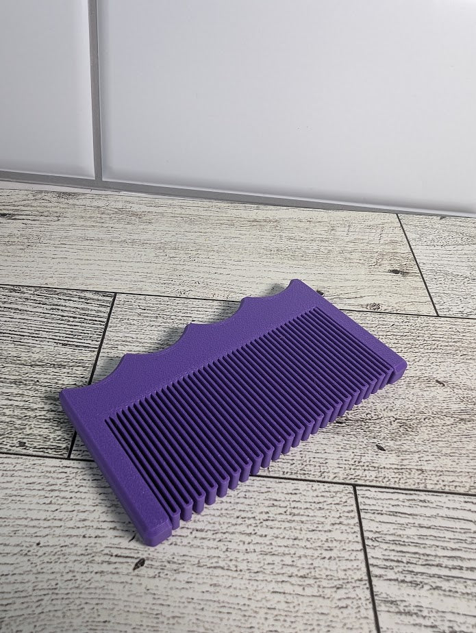 A purple comb is on a light wood grain surface. The backdrop is a white tile