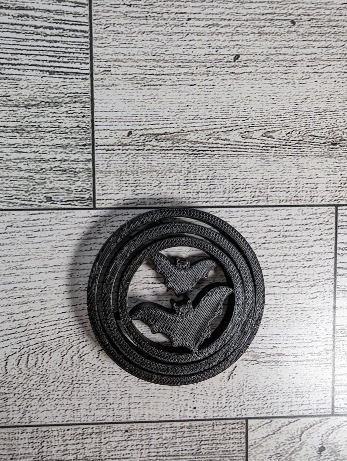 A black circle bat spinner fidget lies flat on a light wood grain