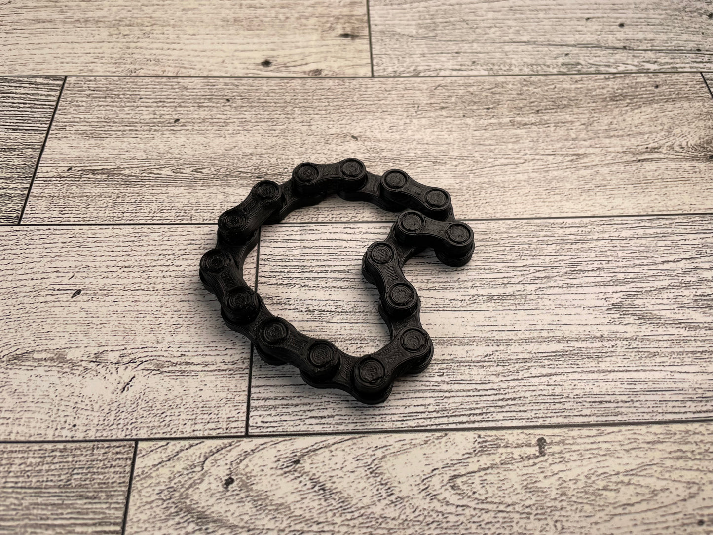 A black chain link on a wood backdrop. The chain is in a heart like shape and there are eight links.