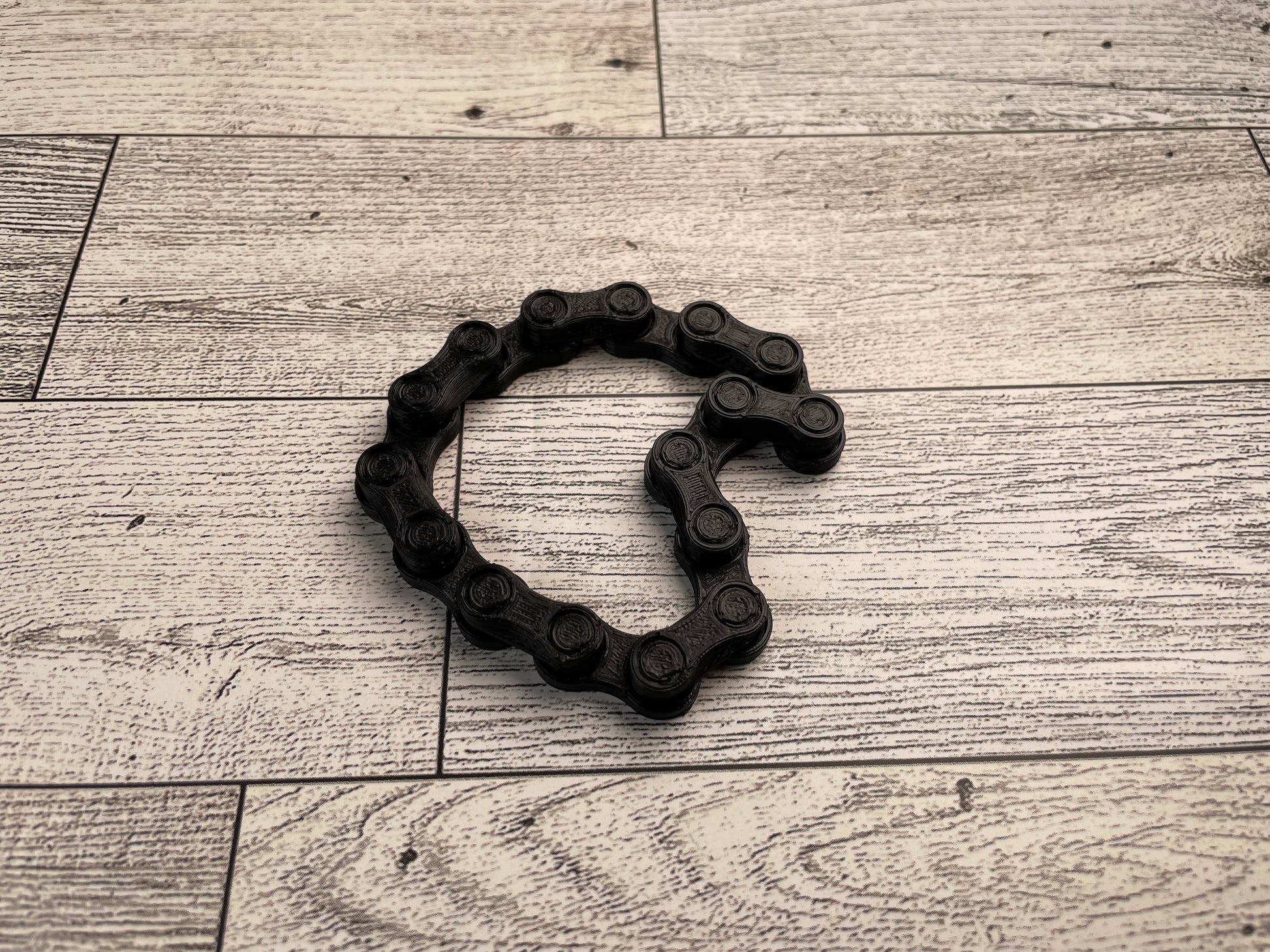 A black chain link on a wood backdrop. The chain is arranged in a squished heart shape and there are eight links.