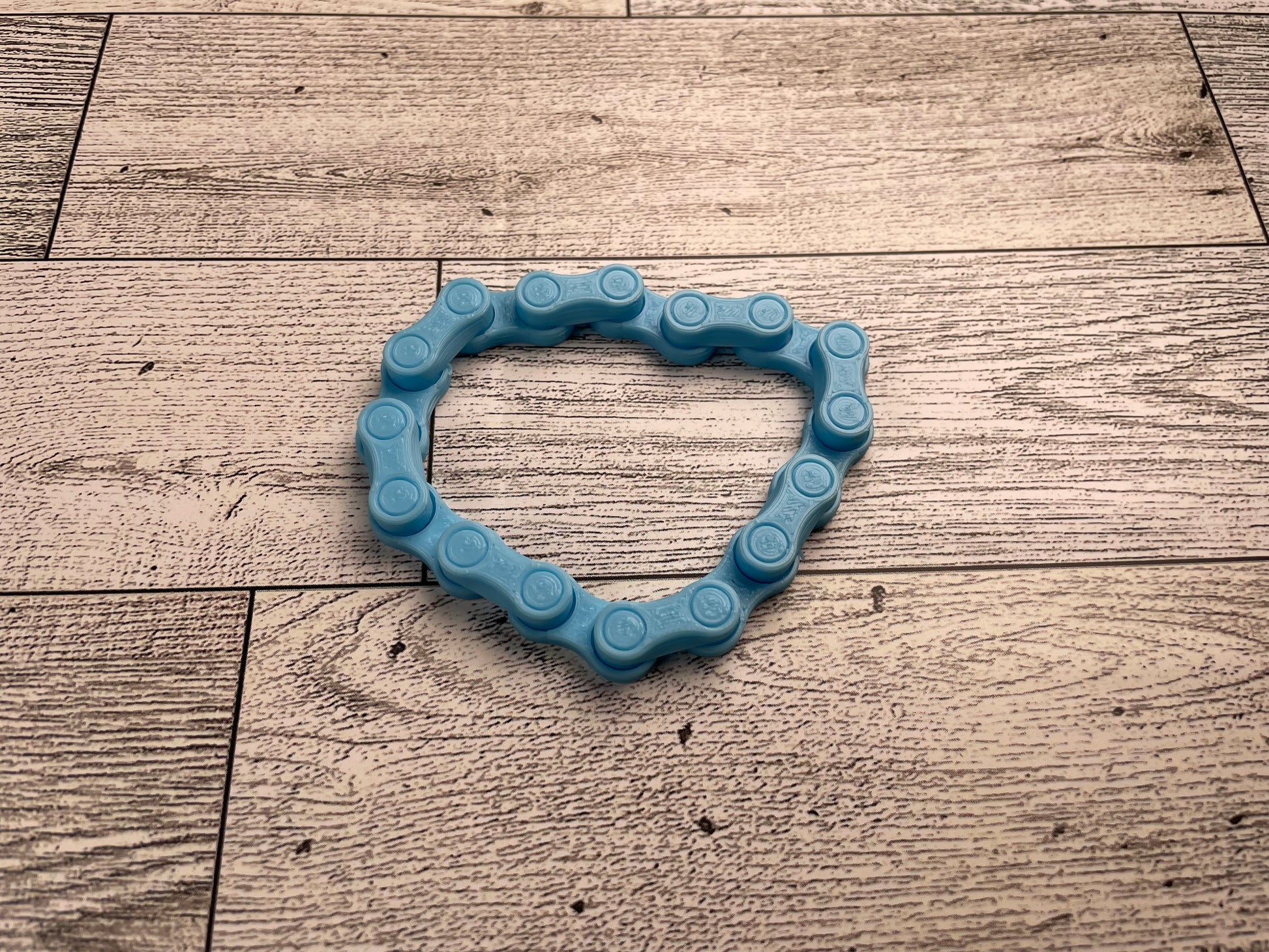 A light blue chain link on a wood backdrop. The chain is arranged in a squished circle and there are eight links.