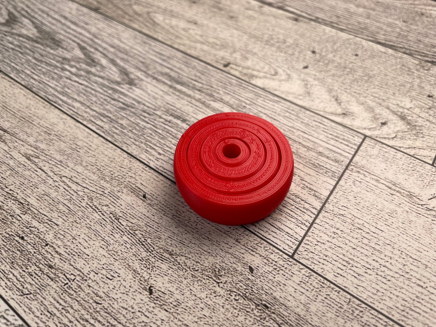 A small 3D printed gyro fidget that is about 1.5 inches in diameter on a wood background. It has four nested circles that can be spun and twirled. It is printed in red filament.