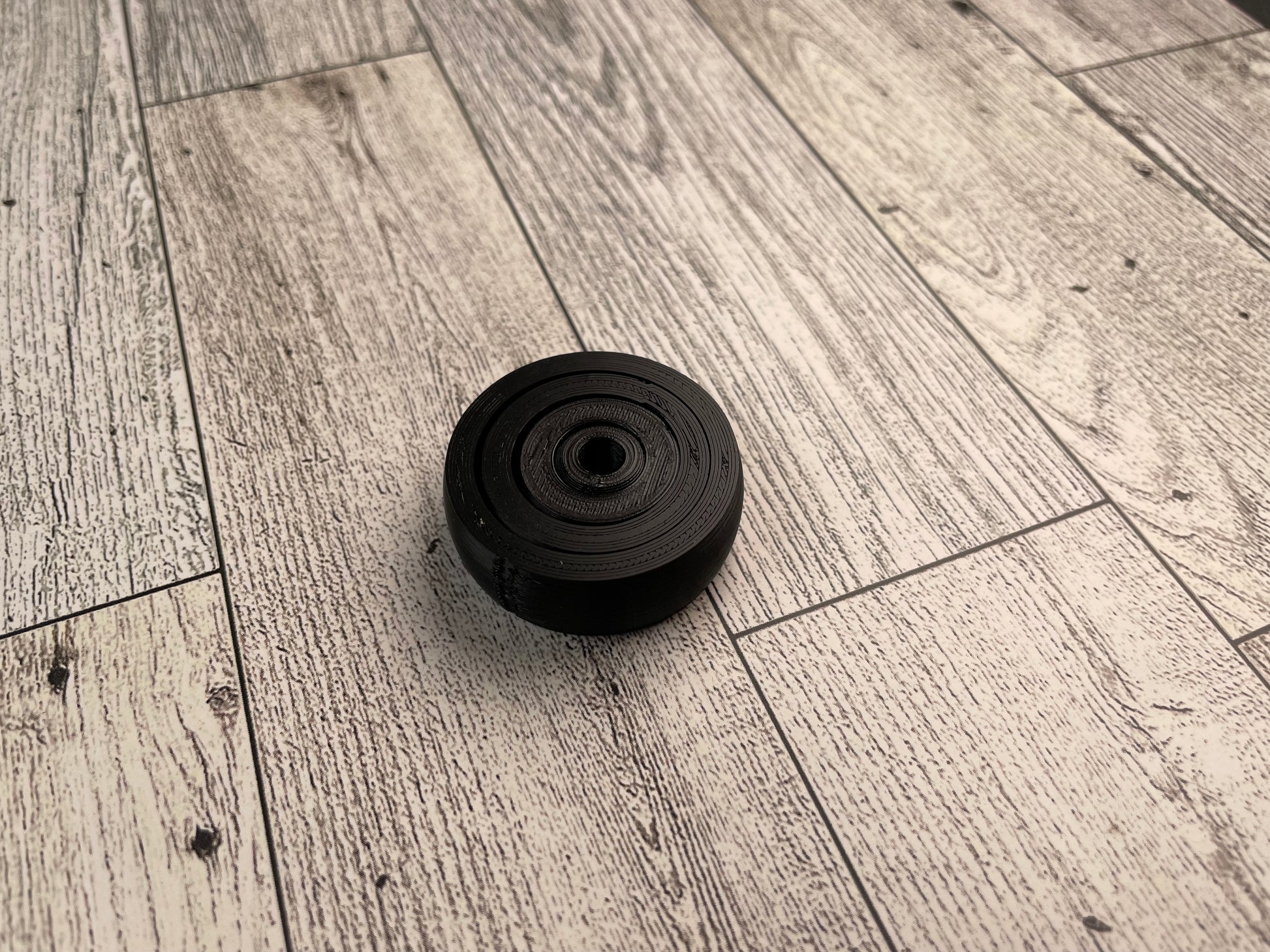A small 3D printed gyro fidget that is about 1.5 inches in diameter on a wood background. It has four nested circles that can be spun and twirled. It is printed in black filament.