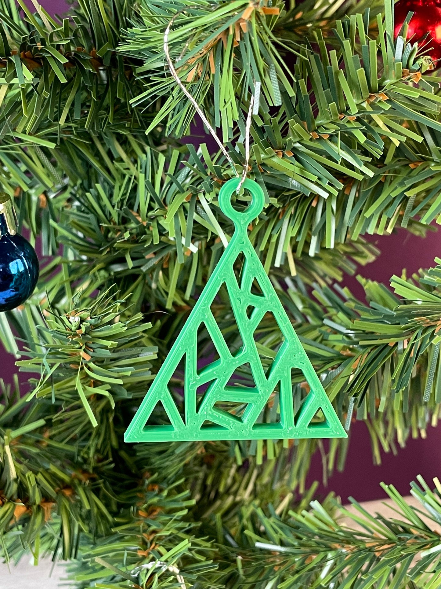 A close up of a fractal tree ornament printed in green filament hung on a christmas tree with a purple background.