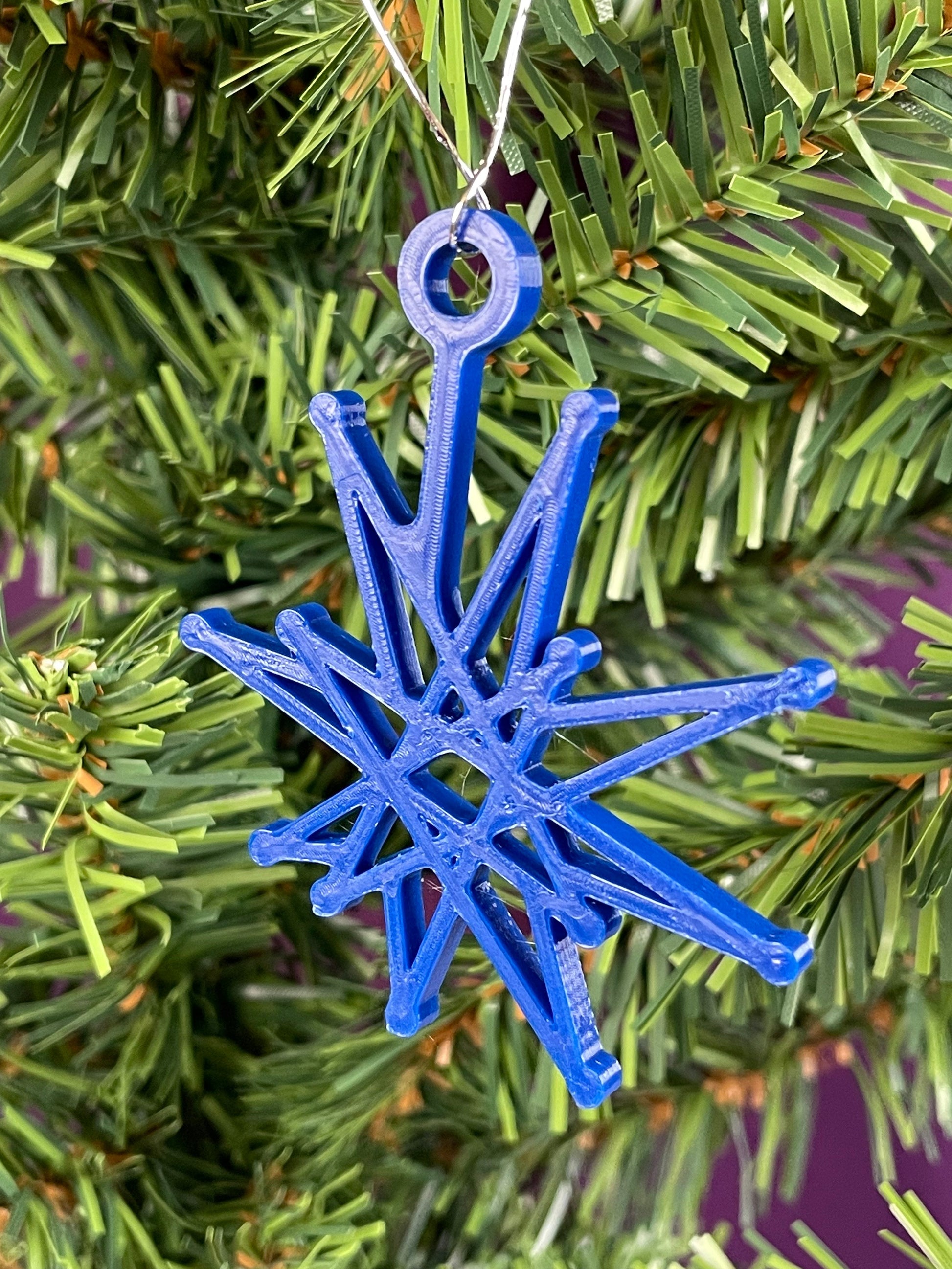 A close up of a fractal starburst ornament hung on a christmas tree with a purple background.