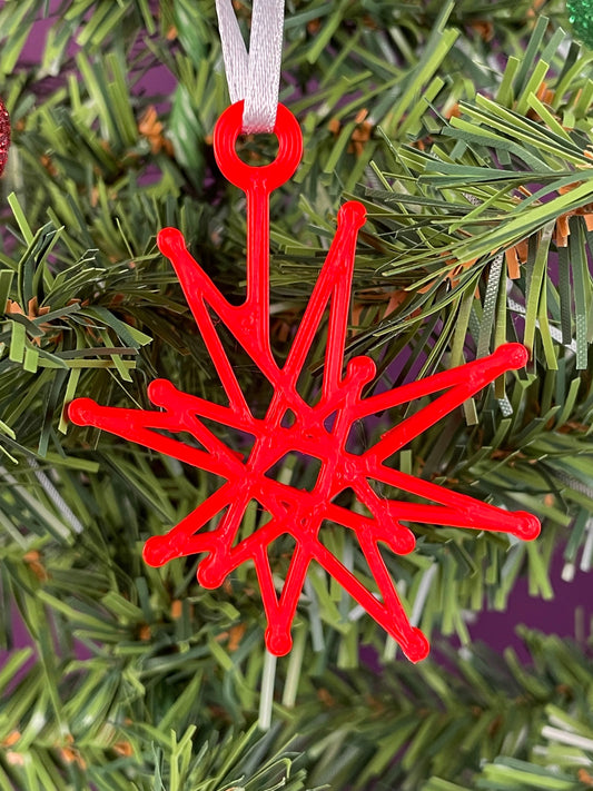 A close up of a fractal starburst ornament printed in red filament hung on a christmas tree with a purple background.
