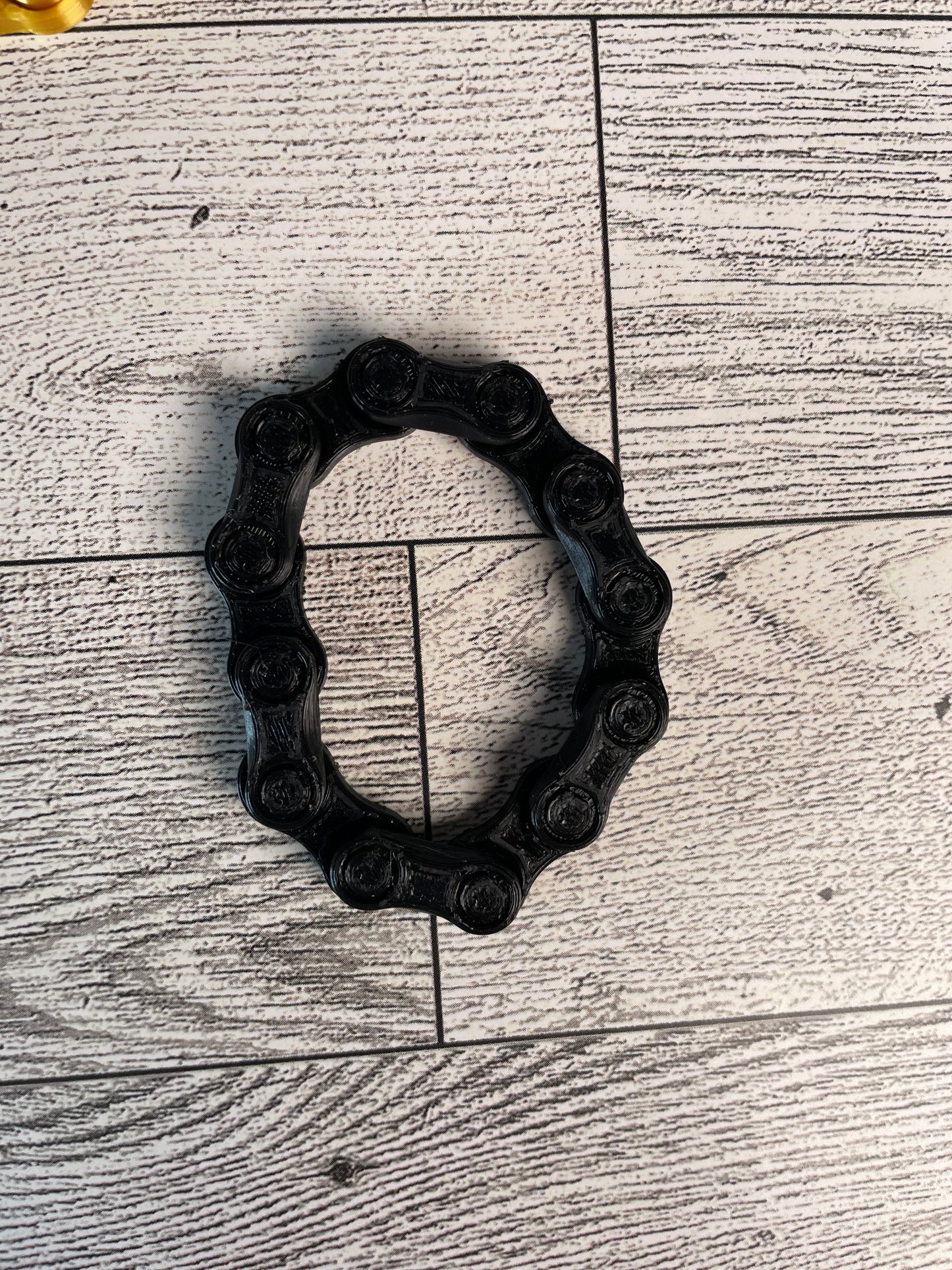 A black chain link on a wood backdrop. The chain is arranged in a oval shape and there are six links.